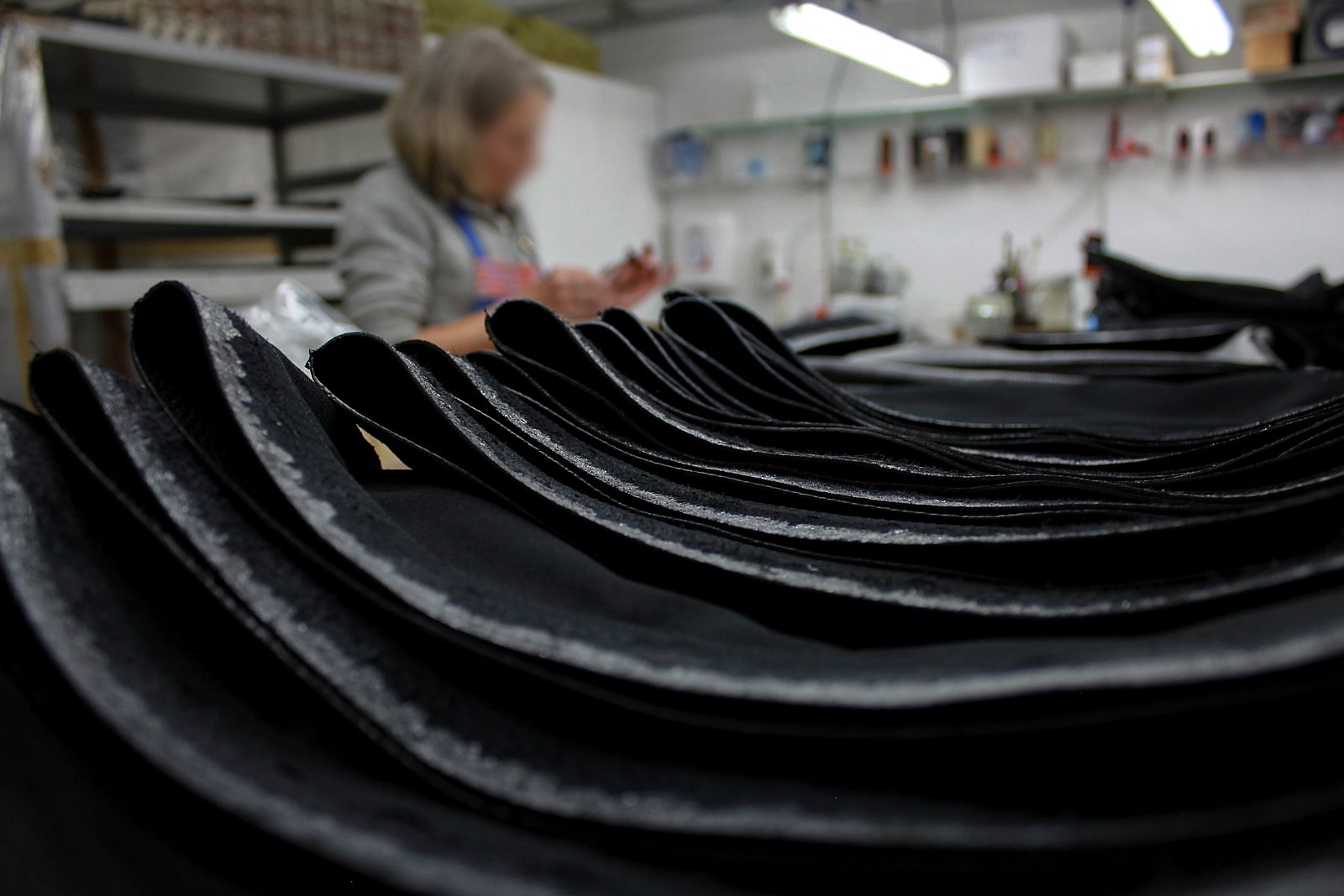 Leather panels stacked in the workshop, a craftswoman at work in the background